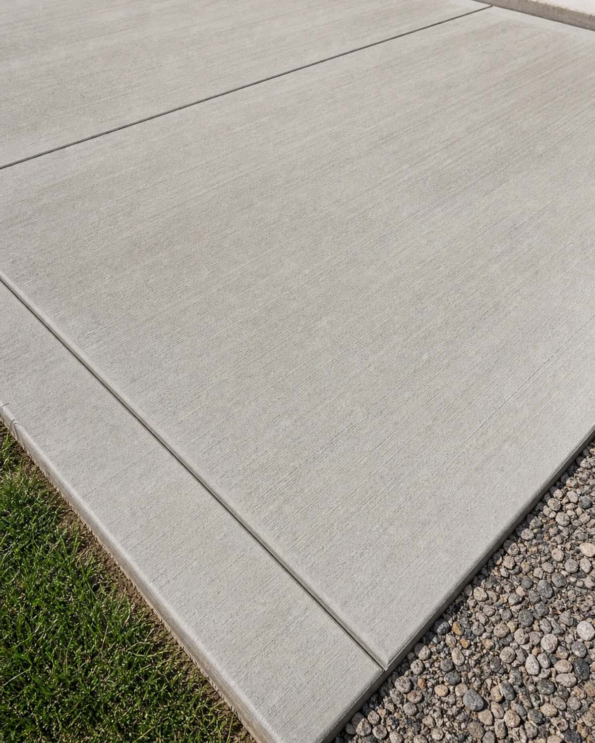 Finished concrete slab or flatwork surface with clean edges, control joints, broom finish, drainage, and realistic texture