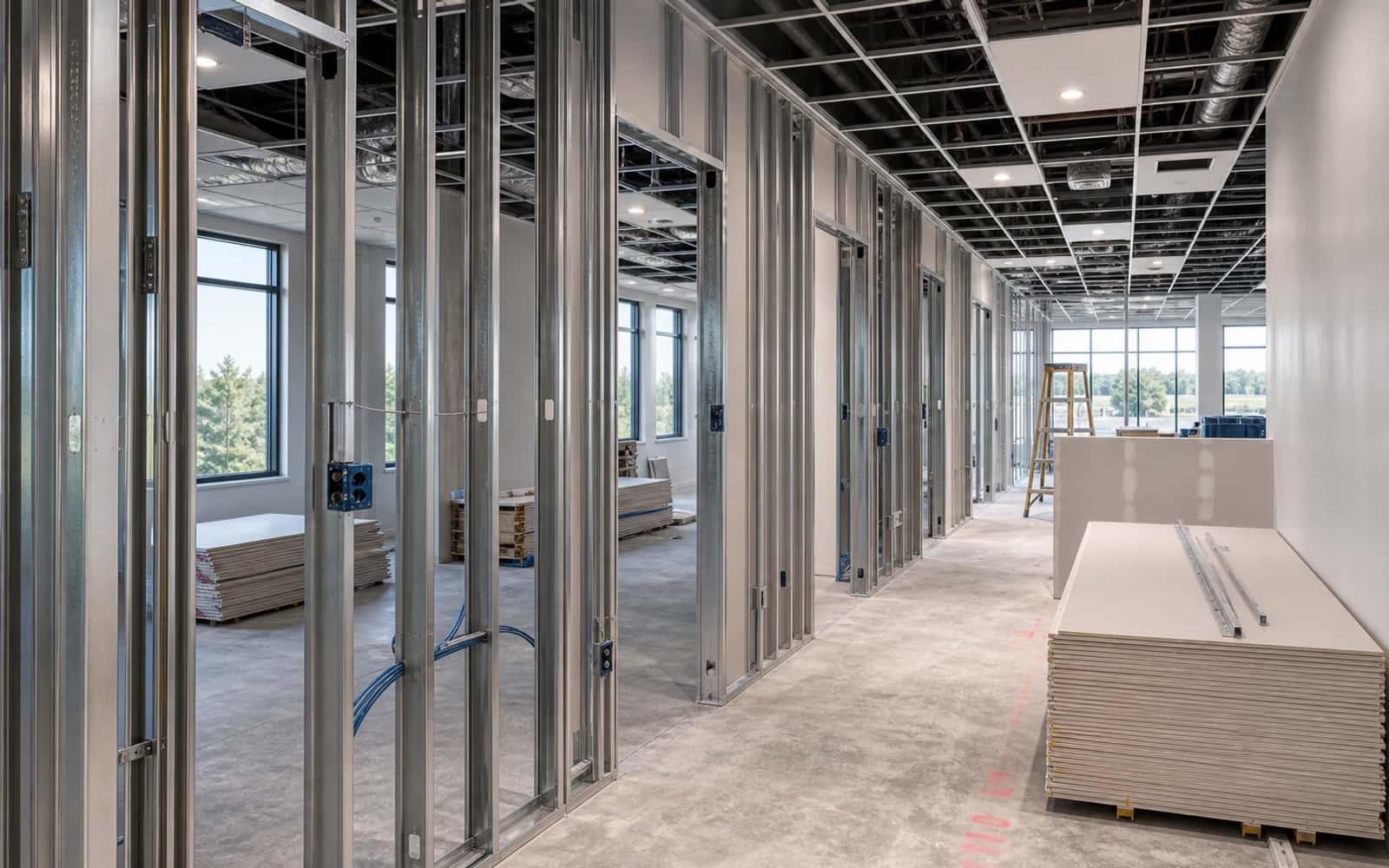 Office buildout in progress with metal framing, data rough-in, ceiling grid, and organized materials
