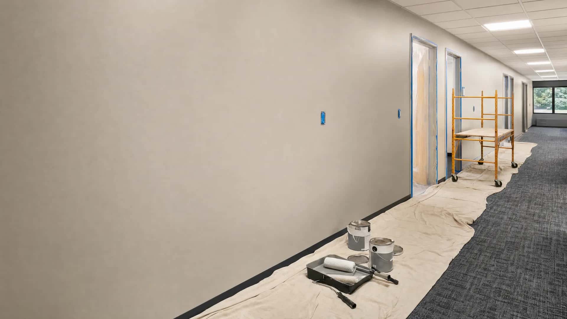 Commercial office corridor repaint in progress with drop cloths, masked frames, and staged equipment.