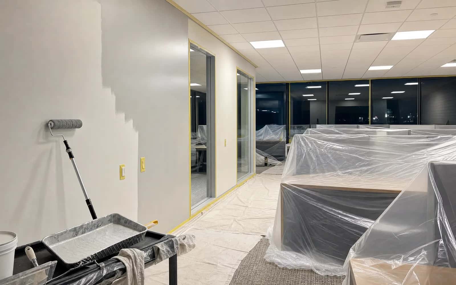 Office area covered and masked for an after-hours repaint with a first coat in progress