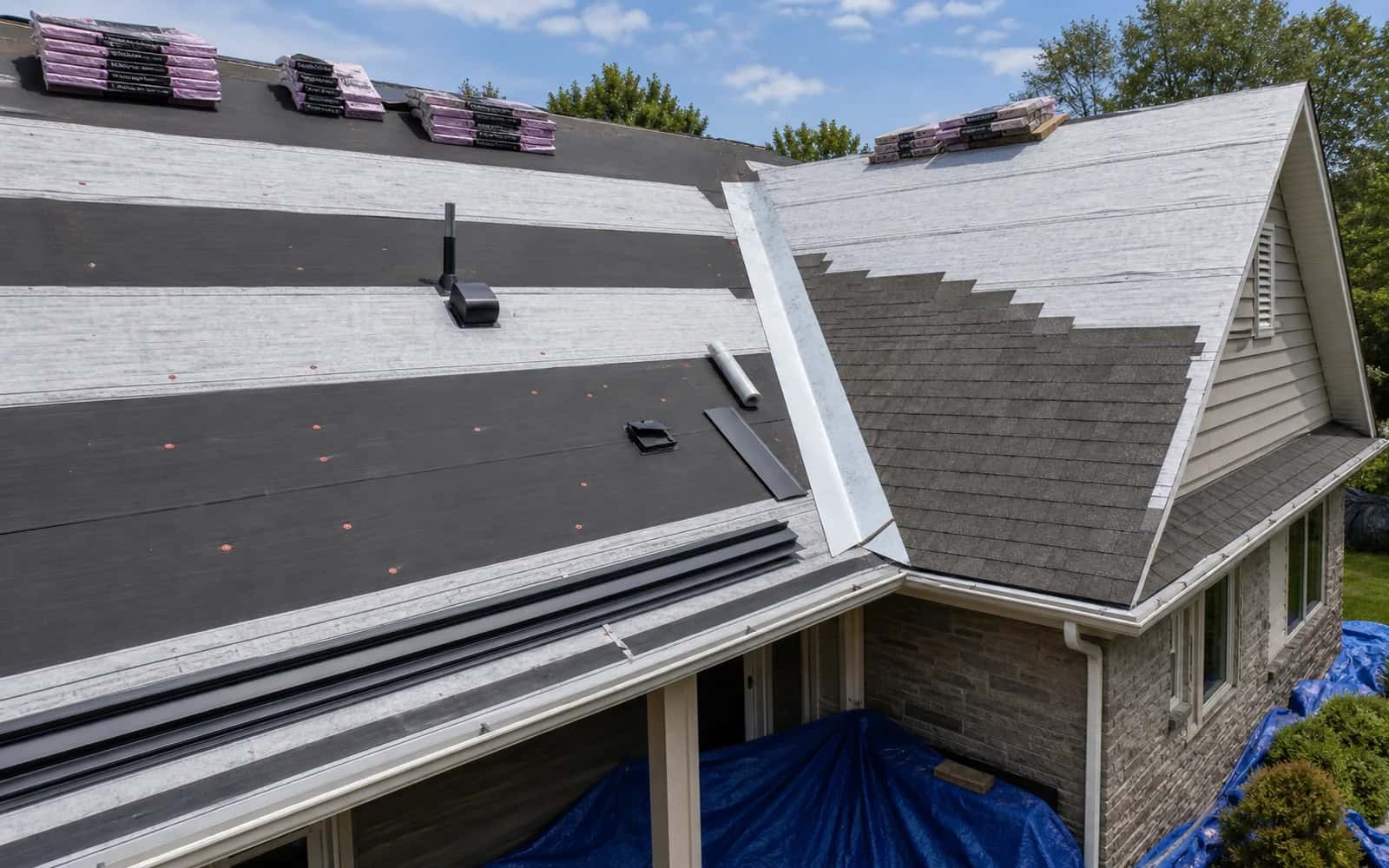 Roof replacement in progress with underlayment, flashing, vents, and staged shingles