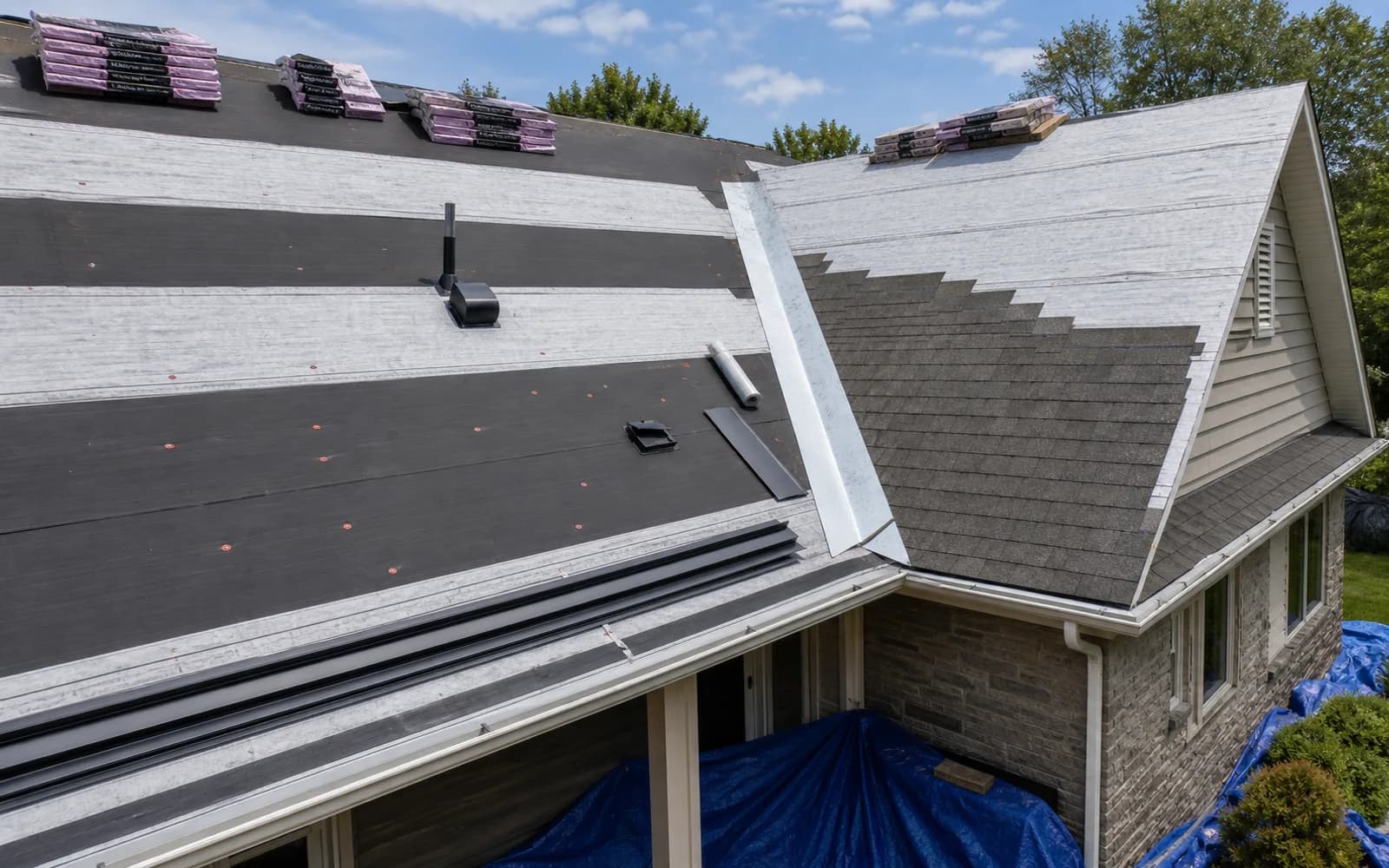 Roof replacement in progress with underlayment, flashing, vents, and staged shingles