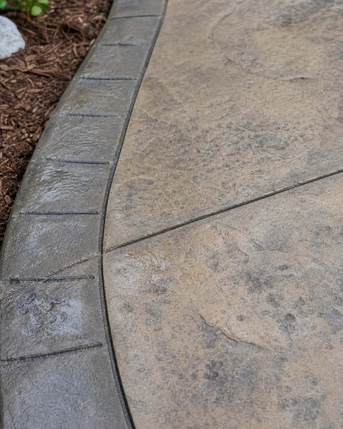 Stamped concrete close detail with texture, border, control joint, color variation, and sealed material surface