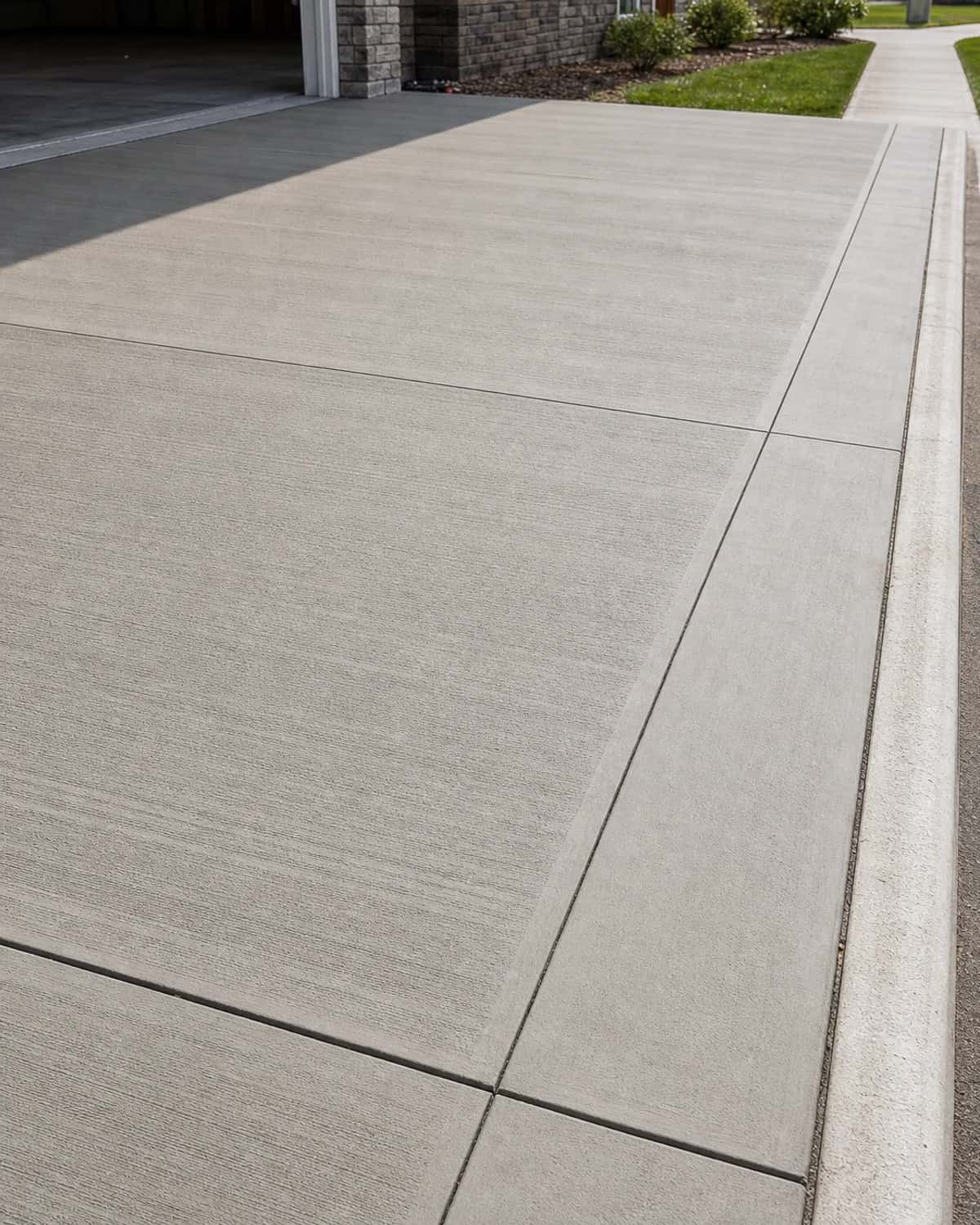Broom-finished concrete driveway edge with clean expansion joint, apron transition, and realistic concrete texture