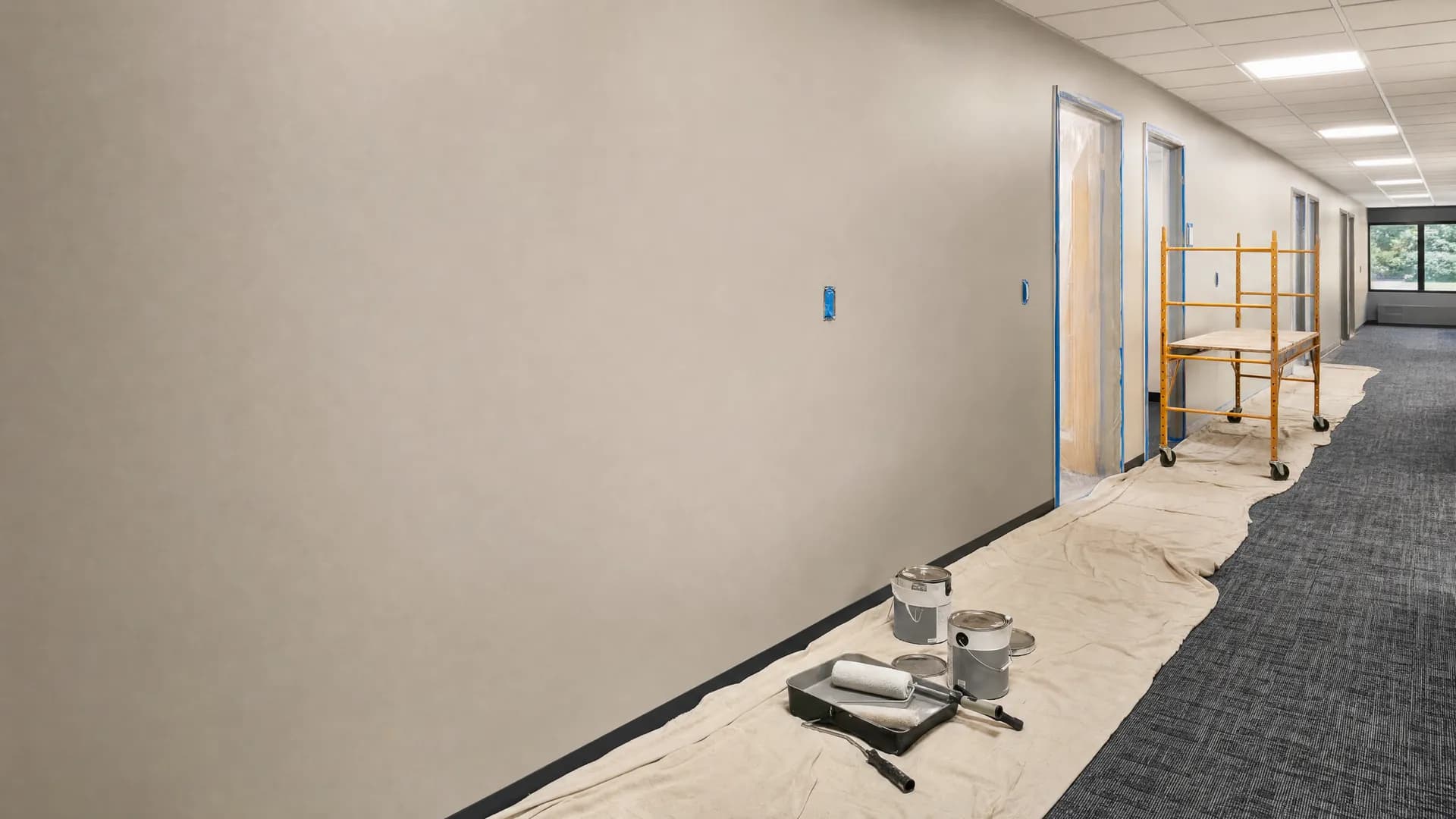 Commercial office corridor repaint in progress with drop cloths, masked frames, and staged equipment.